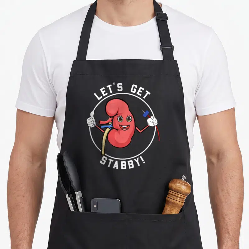 Dialysis kawaii apron - Cartoon red kidney holding a blue-capped needle and thumbs up with arched text — shown on a black cotton canvas apron against a white background