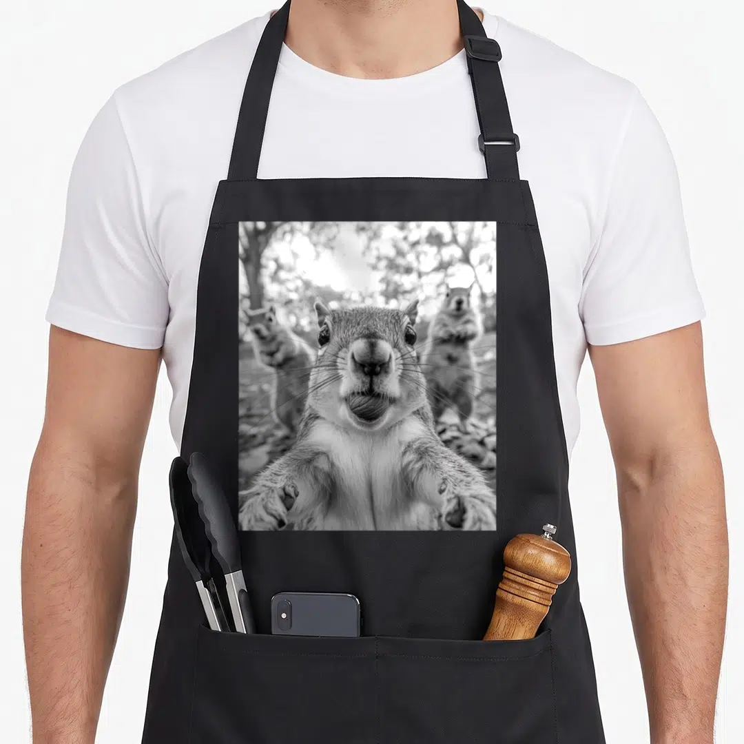Selfie squirrel aprons - Black and white photo of a squirrel holding a nut with two blurred squirrels in the background — shown on a black cotton canvas apron against a white background