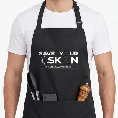 Save melanoma awareness apron - White SAVE YOUR SKIN text with sun icon and black ribbon replacing the I in SKIN above — shown on a black cotton canvas apron against a white background