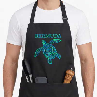 Bermuda travel aprons - Blue and green cartoon sea turtle illustration with BERMUDA text above — shown on a black cotton canvas apron against a white background