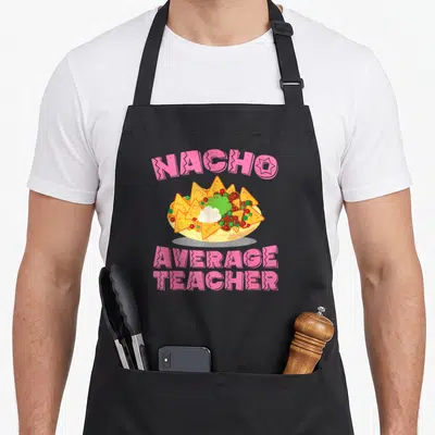 Nacho teacher apron - Pink arched text reading NACHO AVERAGE TEACHER above a cartoon bowl of nachos with green — shown on a black cotton canvas apron against a white background