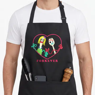 Forky valentine's day apron - Two cartoon forks in pink heart with red ribbon and FORKEVER text below — shown on a black cotton canvas apron against a white background