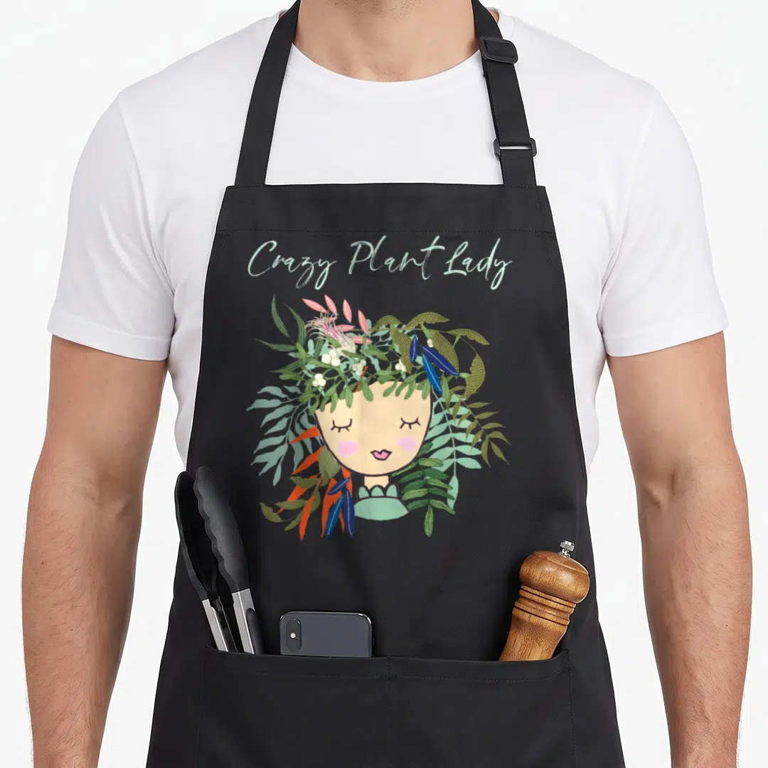 Thumb plant lady apron - Crazy Plant Lady text above cartoon woman with mint, green, blue, and orange leaf crown — shown on a black cotton canvas apron against a white background