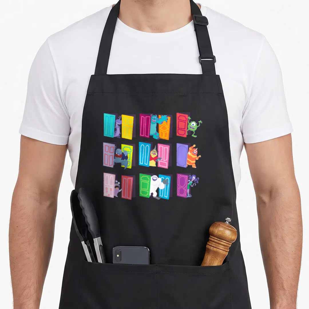 Funny door apron - Nine cartoon monsters standing beside blue red yellow green purple doors in a grid — shown on a black cotton canvas apron against a white background