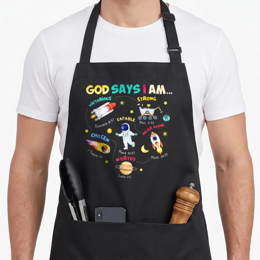 Outer god says i am apron - Watercolor astronaut surrounded by rockets, planets, and bible verses in a circle — shown on a black cotton canvas apron against a white background