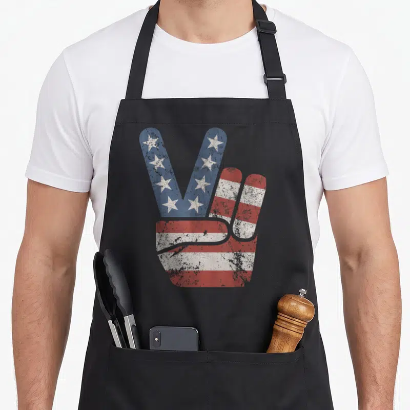 Peace american flag apron - Distressed hand peace sign filled with red white blue stars and stripes pattern — shown on a black cotton canvas apron against a white background