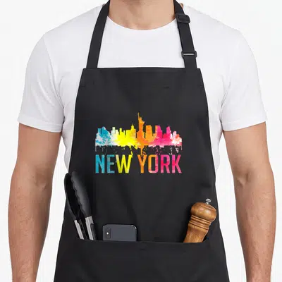 Watercolor new york apron - Colorful NYC skyline watercolor art with paint drips falling onto bold NEW YORK text — shown on a black cotton canvas apron against a white background