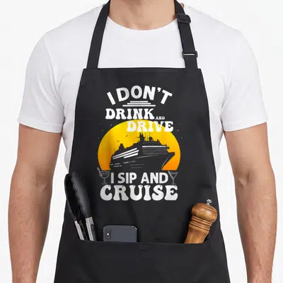 Vacation cruise group humor apron - Retro cruise ship silhouette against yellow sun with cocktail glasses and white pun — shown on a black cotton canvas apron against a white background