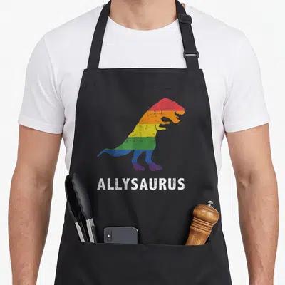Allysaurus dinosaur apron - Rainbow striped T-Rex silhouette above white ALLYSAURUS text on grey background — shown on a black cotton canvas apron against a white background