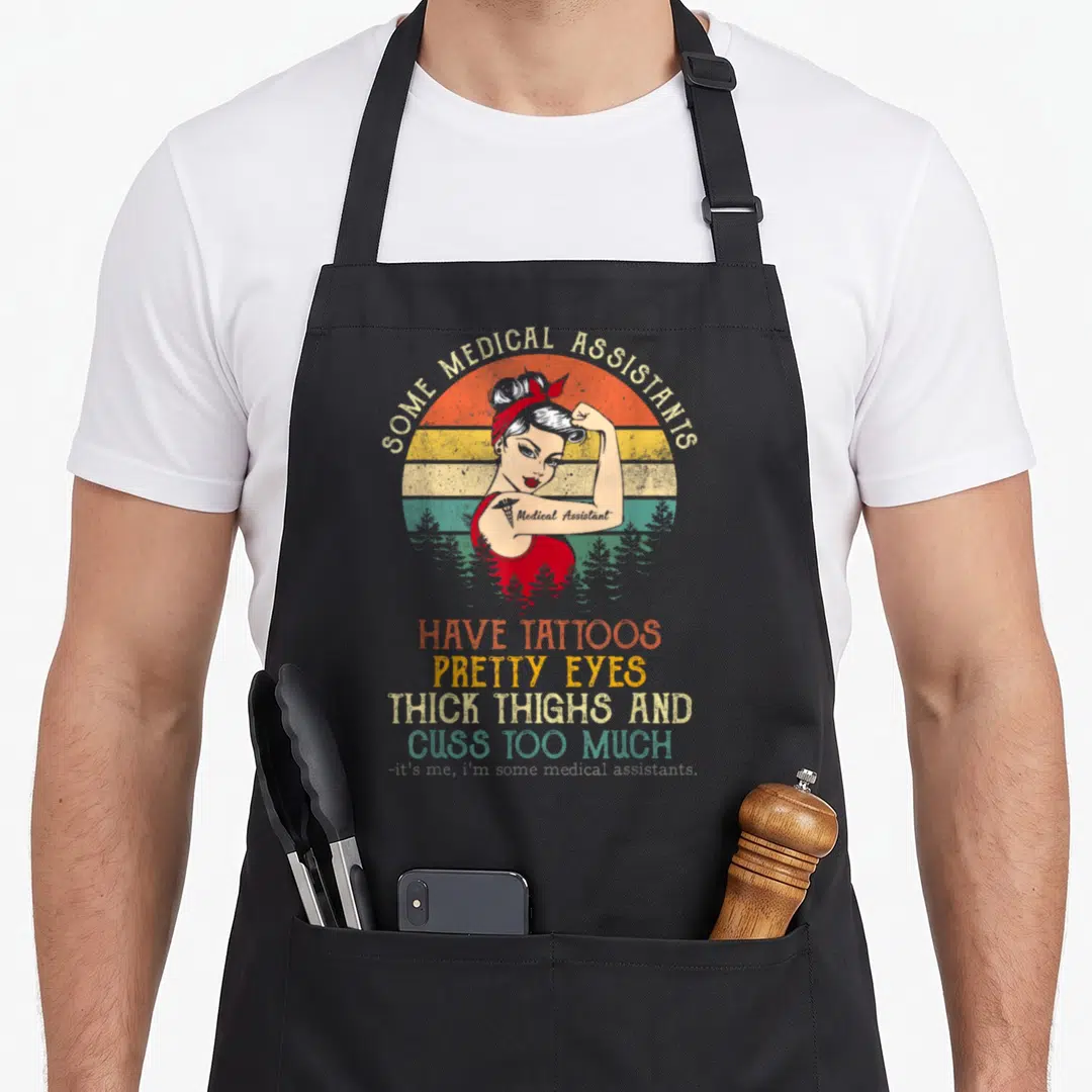 Medical tattoo apron - Retro pin-up woman flexing arm with tattoo against striped sunset and stacked humorous text — shown on a black cotton canvas apron against a white background