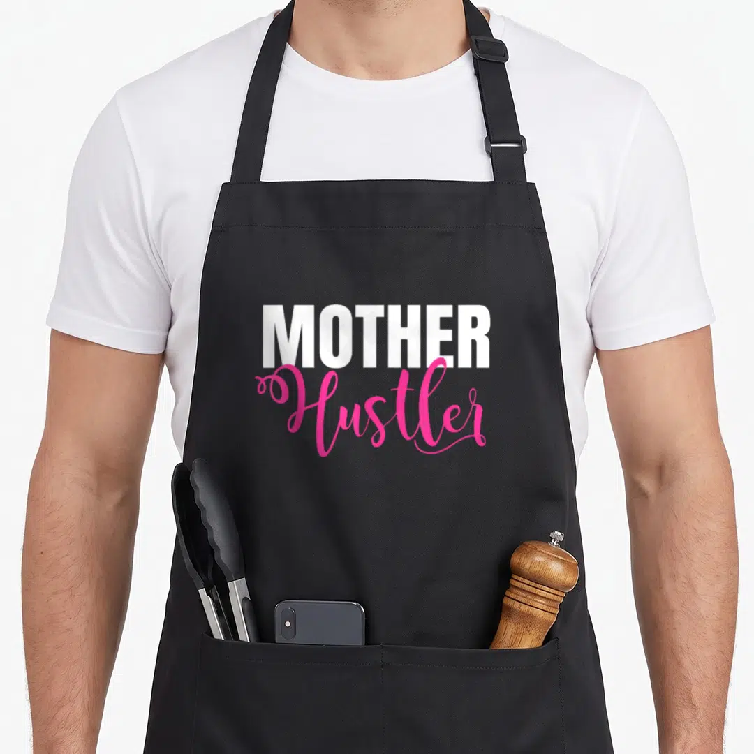 Hustler mother's apron - Stacked white MOTHER and pink Hustler text on a black background — shown on a black cotton canvas apron against a white background