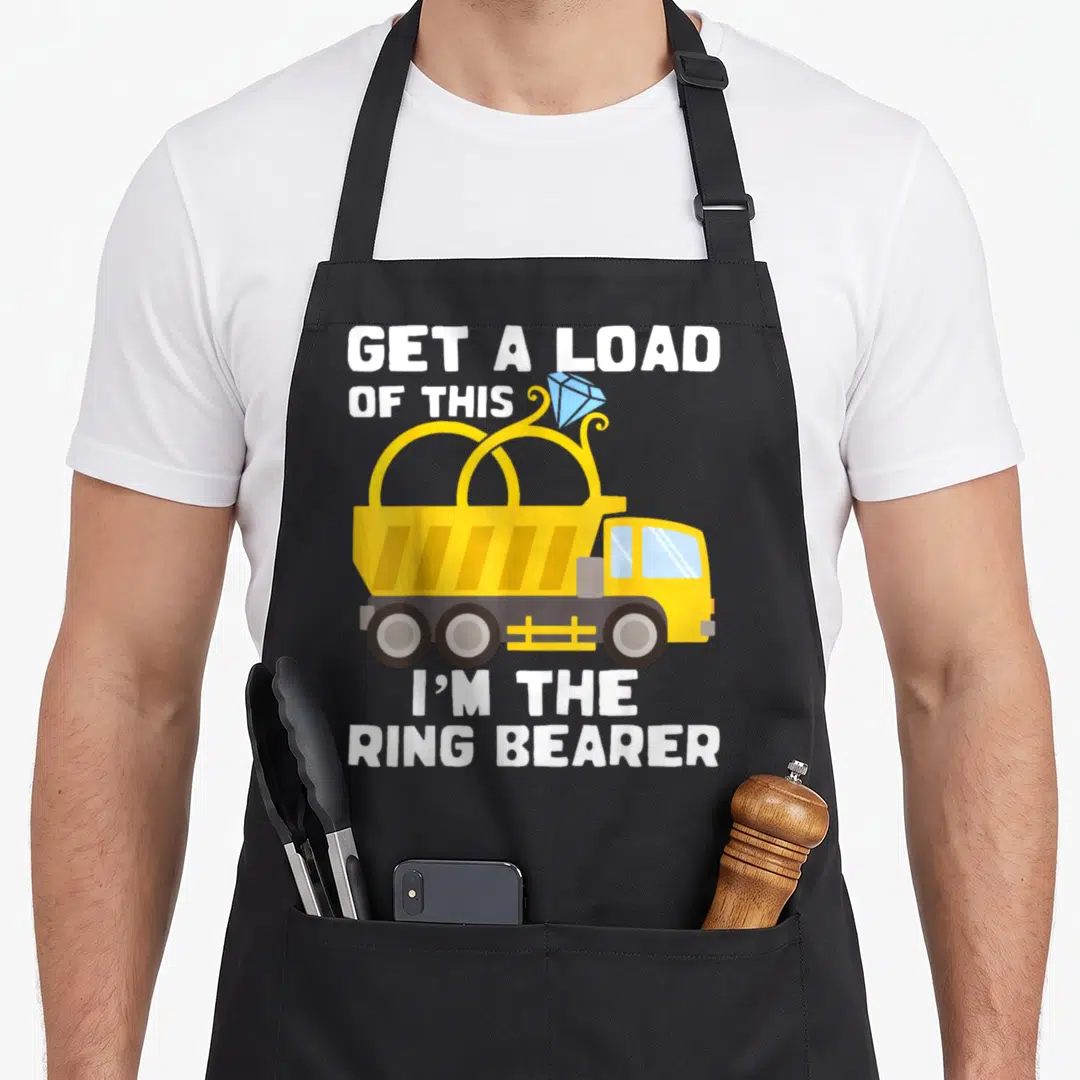 Bearer ring apron - Yellow dump truck carrying blue diamond ring with white text GET A LOAD OF THIS I'M THE RING BEARER — shown on a black cotton canvas apron against a white background
