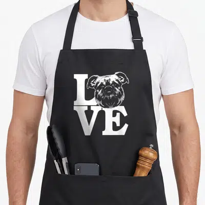 Brussel i love my vulture apron - White dog head illustration replacing the letter O in stacked LOVE text — shown on a black cotton canvas apron against a white background