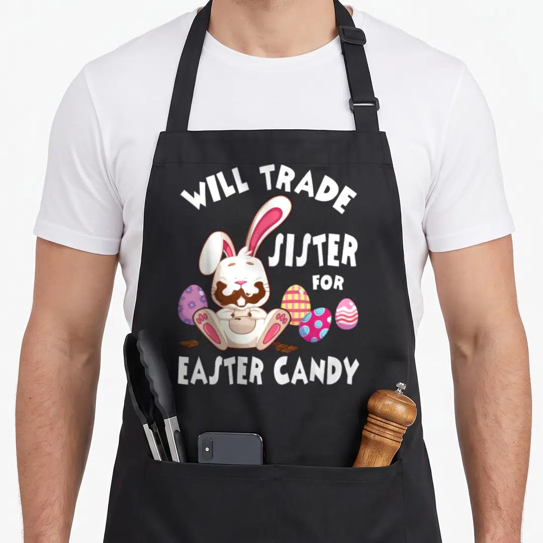 Eat easter bunny aprons - Cartoon bunny with chocolate face surrounded by eggs and text Will Trade Sister For Easter — shown on a black cotton canvas apron against a white background