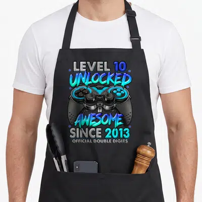 10th birthday gaming aprons - Game controller with LEVEL 10 UNLOCKED AWESOME SINCE 2013 text in black blue and cyan — shown on a black cotton canvas apron against a white background