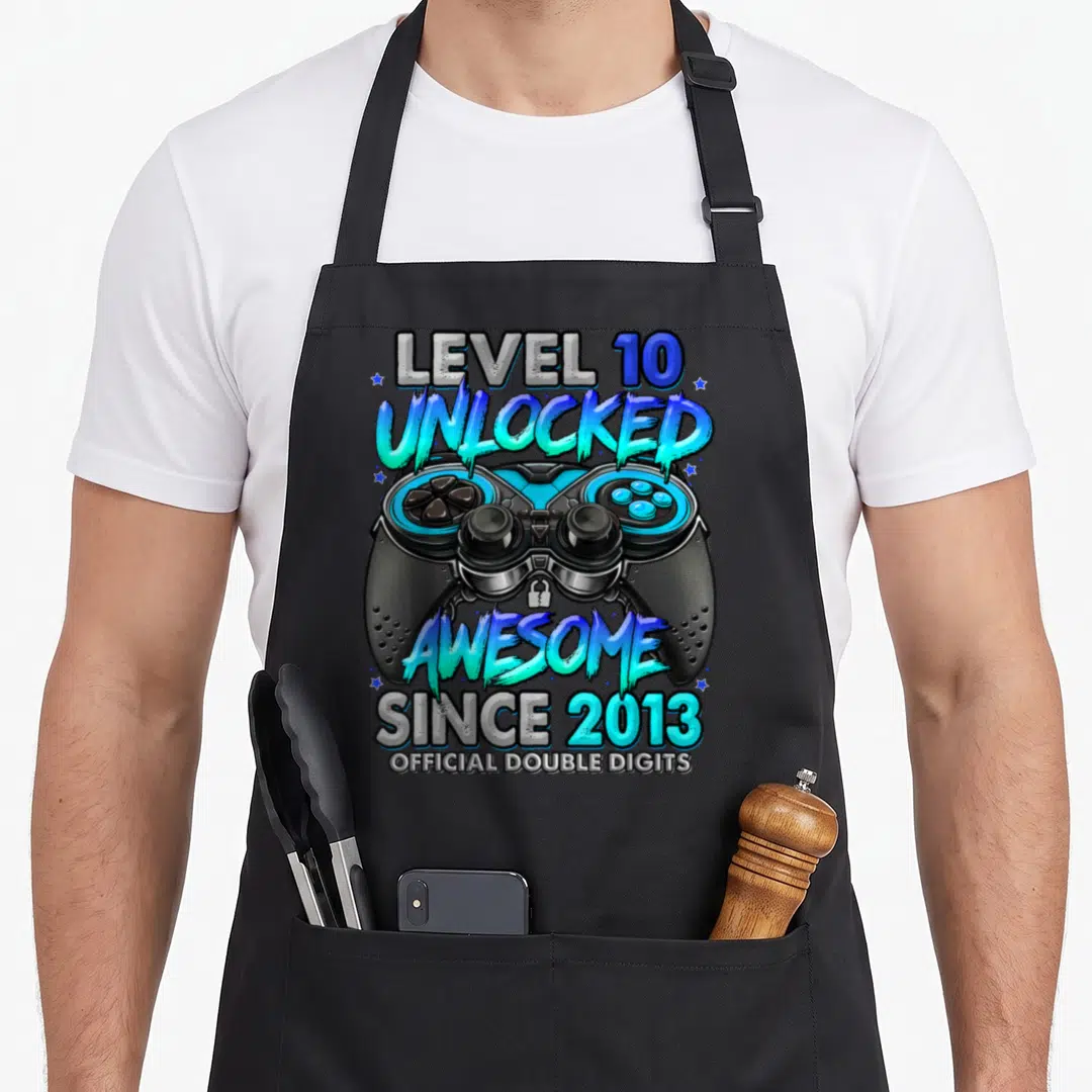 10th birthday gaming aprons - Game controller with LEVEL 10 UNLOCKED AWESOME SINCE 2013 text in black blue and cyan — shown on a black cotton canvas apron against a white background