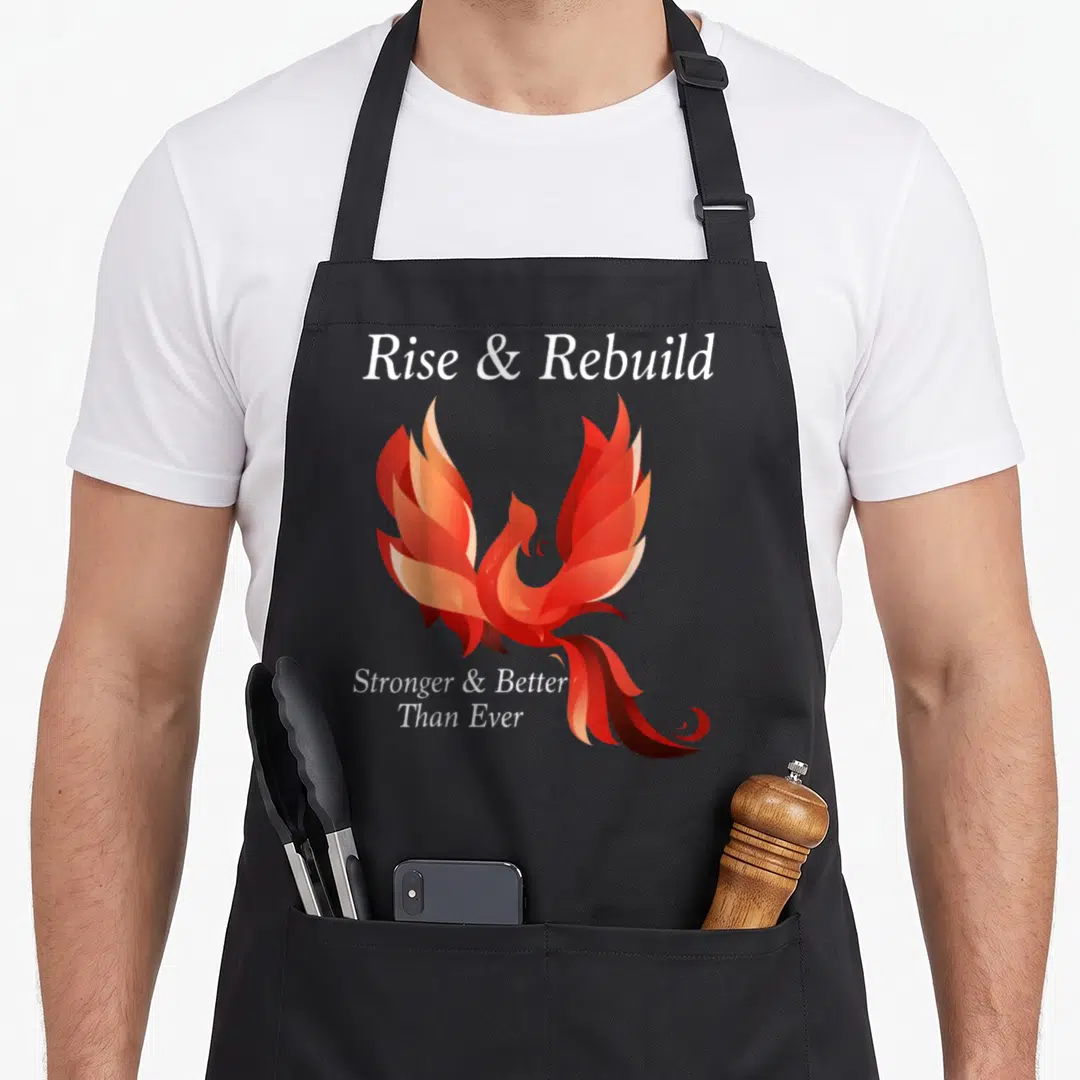 Rise bird apron - Realistic red and orange phoenix between Rise Rebuild and Stronger Better Than Ever text — shown on a black cotton canvas apron against a white background