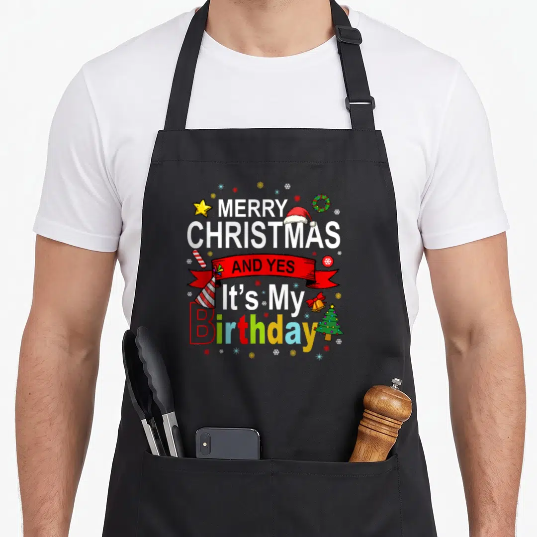 Birthday merry christmas apron - Stacked Merry Christmas and Yes Its My Birthday text with Santa hat and tree icons — shown on a black cotton canvas apron against a white background