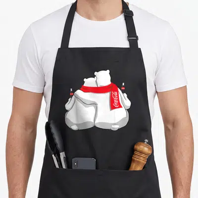 Coca holiday apron - Two polar bears from behind with red scarf and soda bottles, Coca-Cola text visible — shown on a black cotton canvas apron against a white background