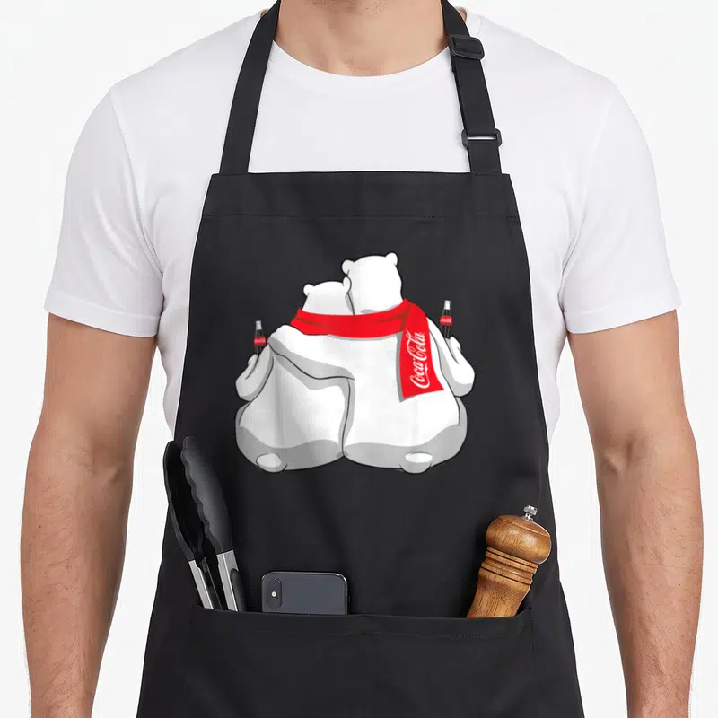 Coca holiday apron - Two polar bears from behind with red scarf and soda bottles, Coca-Cola text visible — shown on a black cotton canvas apron against a white background