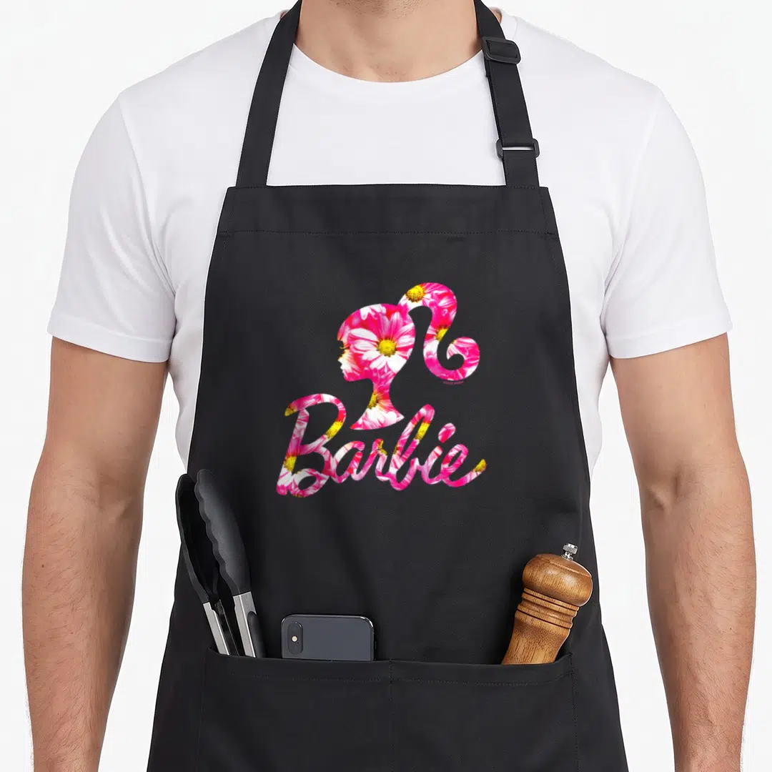 Retro daisy apron - Barbie silhouette and script text filled with pink white and yellow floral pattern — shown on a black cotton canvas apron against a white background