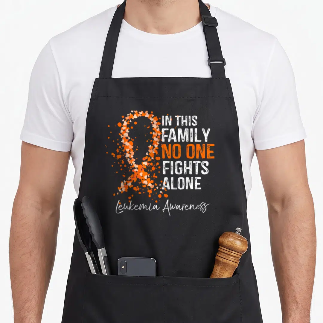Fight family aprons - Heart ribbon and IN THIS FAMILY NO ONE FIGHTS ALONE text in white and orange distressed print — shown on a black cotton canvas apron against a white background