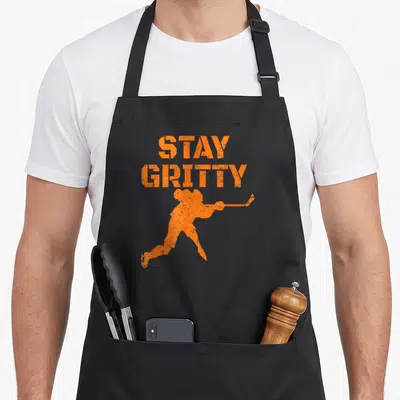 Stay phillies apron - Orange distressed STAY GRITTY text above hockey player silhouette holding stick — shown on a black cotton canvas apron against a white background