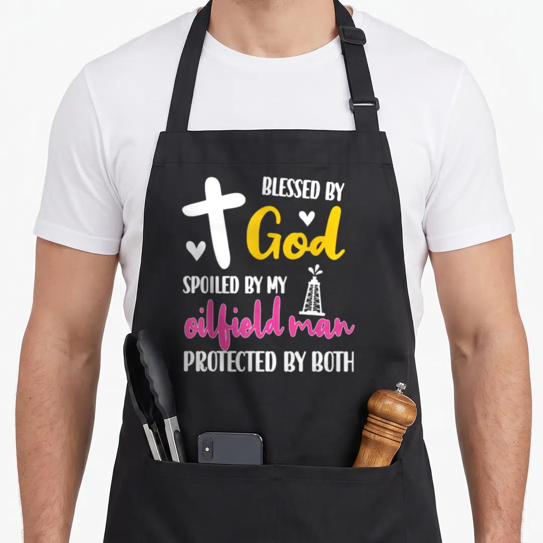 Oilfield husband wife aprons - Cross and oil derrick graphic with text Blessed by God Spoiled by My Oilfield Man — shown on a black cotton canvas apron against a white background