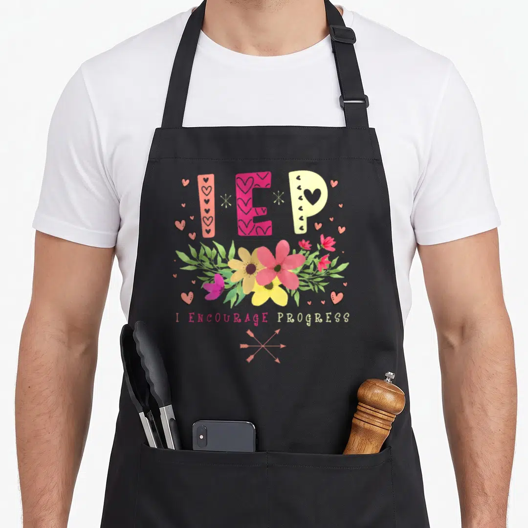 Special education teacher apron - IEP letters above pink yellow and white flowers with crossed arrows and text — shown on a black cotton canvas apron against a white background