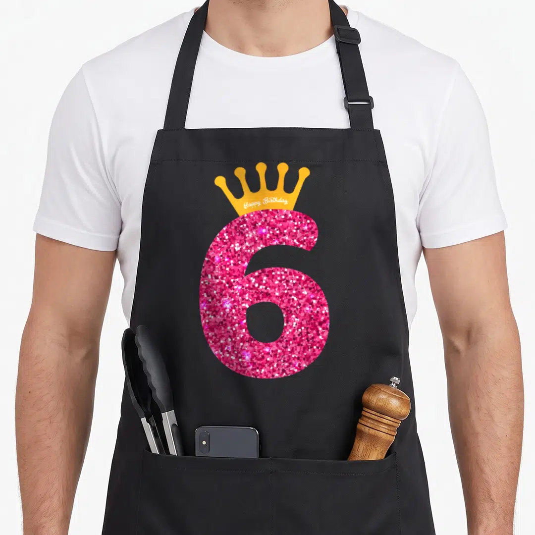 6th bday birthday apron - Pink glitter number 6 with orange crown and white Happy Birthday text in cartoon style — shown on a black cotton canvas apron against a white background