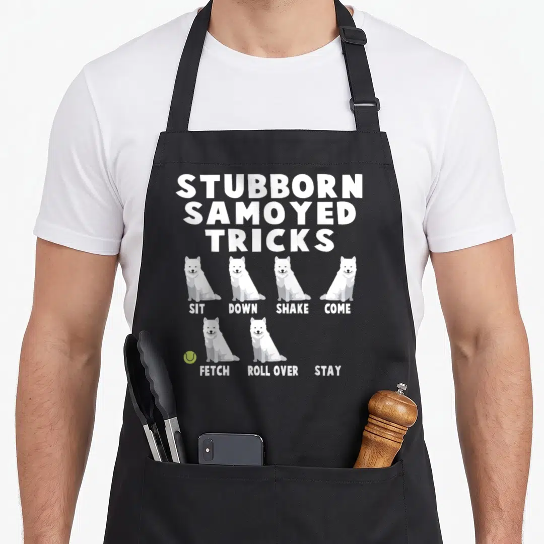 Stubborn samoyed apron - Cartoon Samoyeds listed under stubborn tricks with a lime green tennis ball — shown on a black cotton canvas apron against a white background