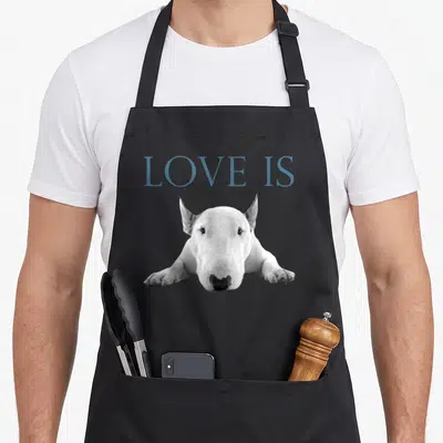 Funny bull terrier loves apron - Blue-grey LOVE IS text above a white bull terrier dog lying down on grey background — shown on a black cotton canvas apron against a white background