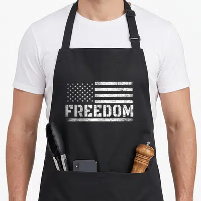 Freedom american flag apron - Distressed white USA flag above the word FREEDOM printed on canvas — shown on a black cotton canvas apron against a white background