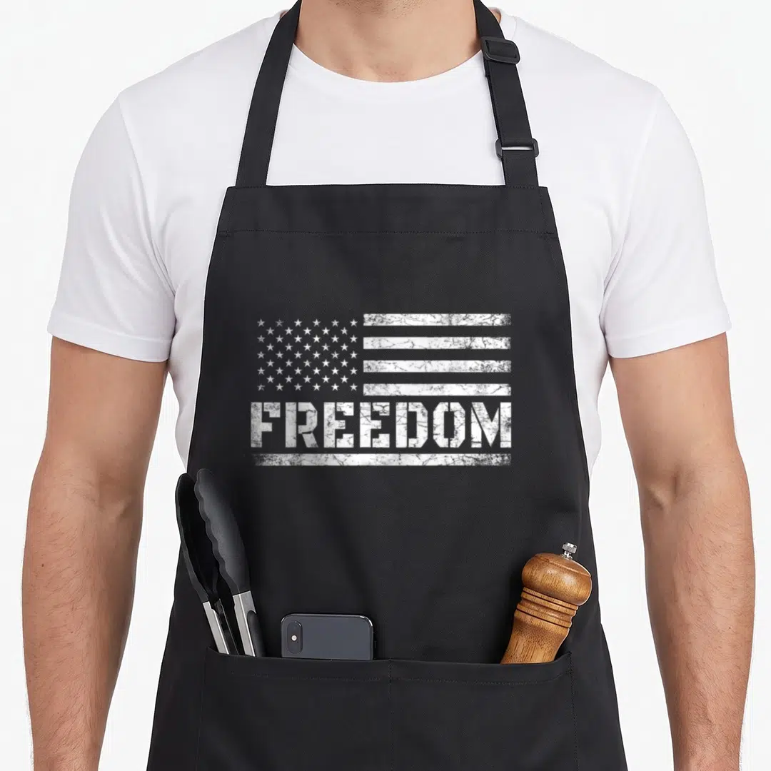 Freedom american flag apron - Distressed white USA flag above the word FREEDOM printed on canvas — shown on a black cotton canvas apron against a white background