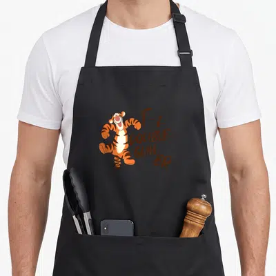 Tigger lunar apron - Leaping orange tiger next to stacked brown text reading T-I-DOUBLE-GUH-ER — shown on a black cotton canvas apron against a white background
