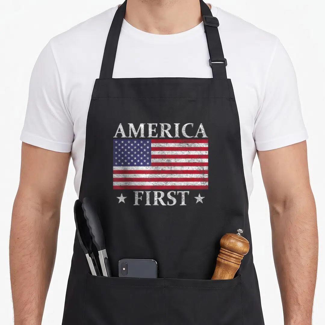 Stripe american flag apron - Distressed USA flag with AMERICA above and FIRST below flanked by two white stars on black — shown on a black cotton canvas apron against a white background