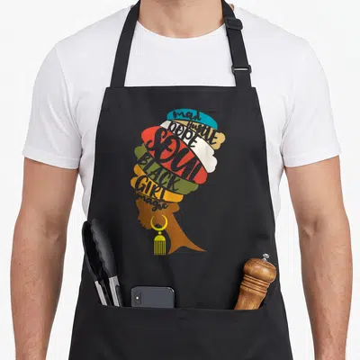 Mad magic apron - Woman profile silhouette composed of colorful text shapes reading mad Hustle DOPE SOUL BLACK GIRL — shown on a black cotton canvas apron against a white background