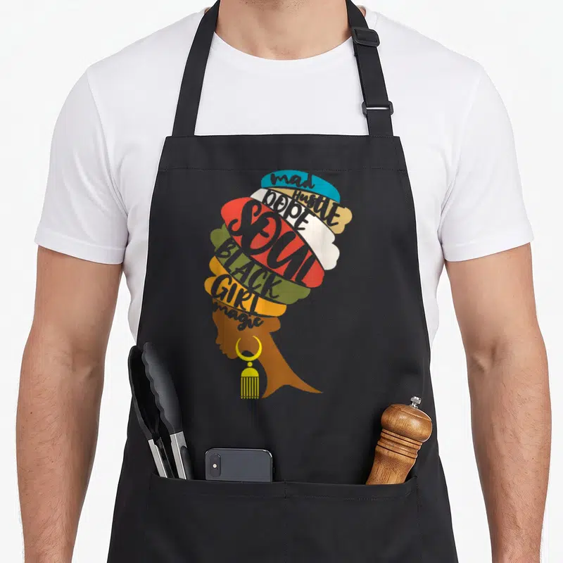 Mad magic apron - Woman profile silhouette composed of colorful text shapes reading mad Hustle DOPE SOUL BLACK GIRL — shown on a black cotton canvas apron against a white background