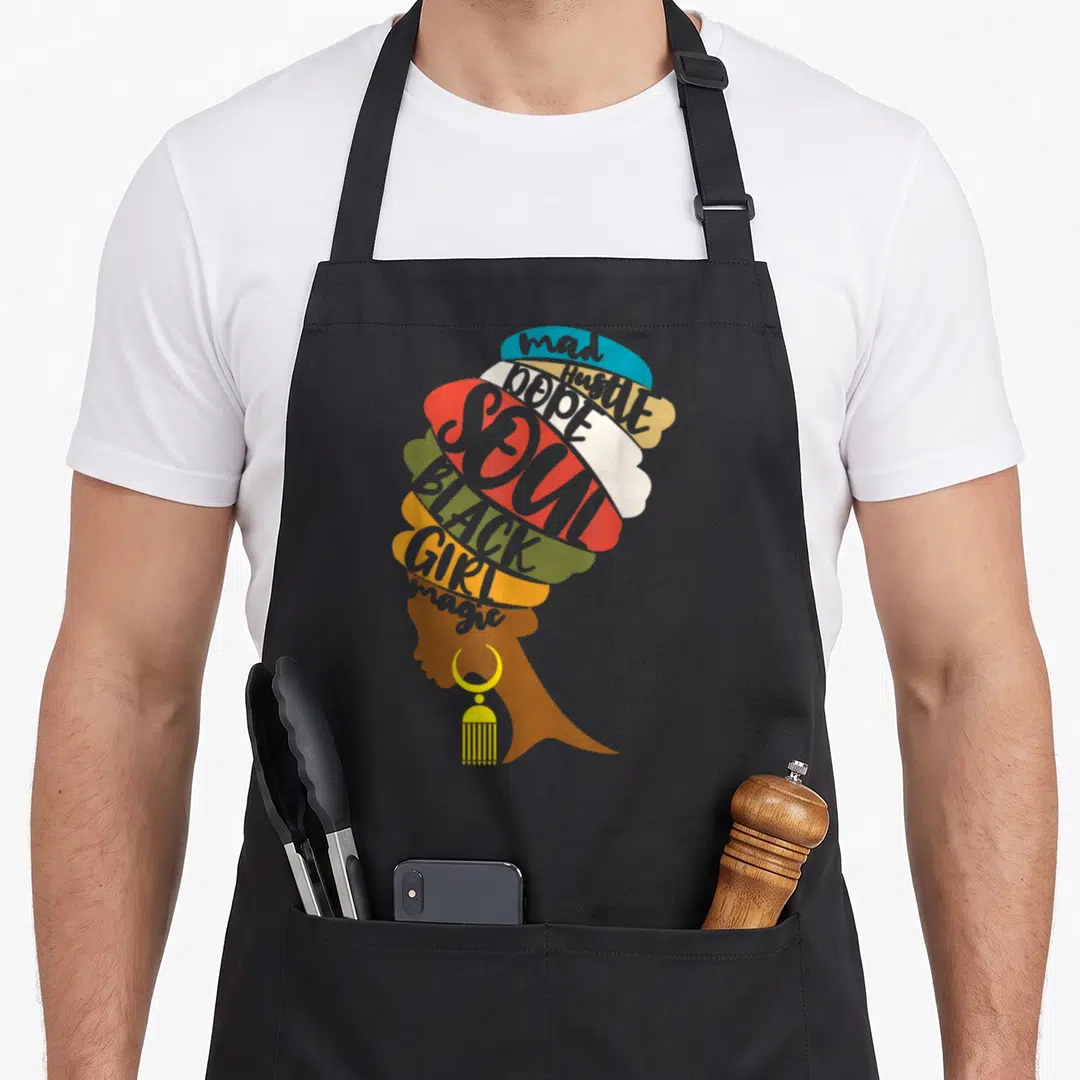 Mad magic apron - Woman profile silhouette composed of colorful text shapes reading mad Hustle DOPE SOUL BLACK GIRL — shown on a black cotton canvas apron against a white background
