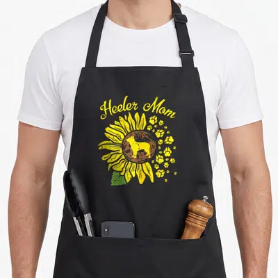 Australian dog apron - Heeler Mom text over yellow sunflower with dog silhouette and paw prints — shown on a black cotton canvas apron against a white background