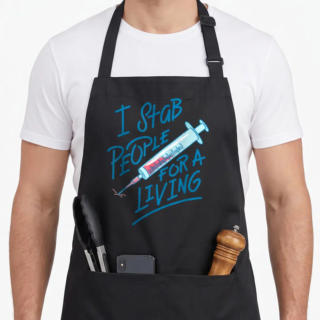 Stab nurse apron - Cartoon syringe with pink fluid and blue text I STAB PEOPLE FOR A LIVING — shown on a black cotton canvas apron against a white background
