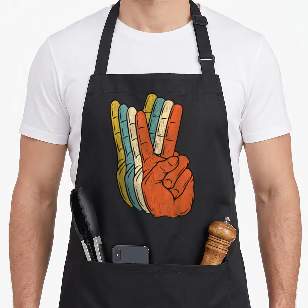 Peace hippie apron - Retro hand making peace sign in yellow blue beige and orange layers — shown on a black cotton canvas apron against a white background