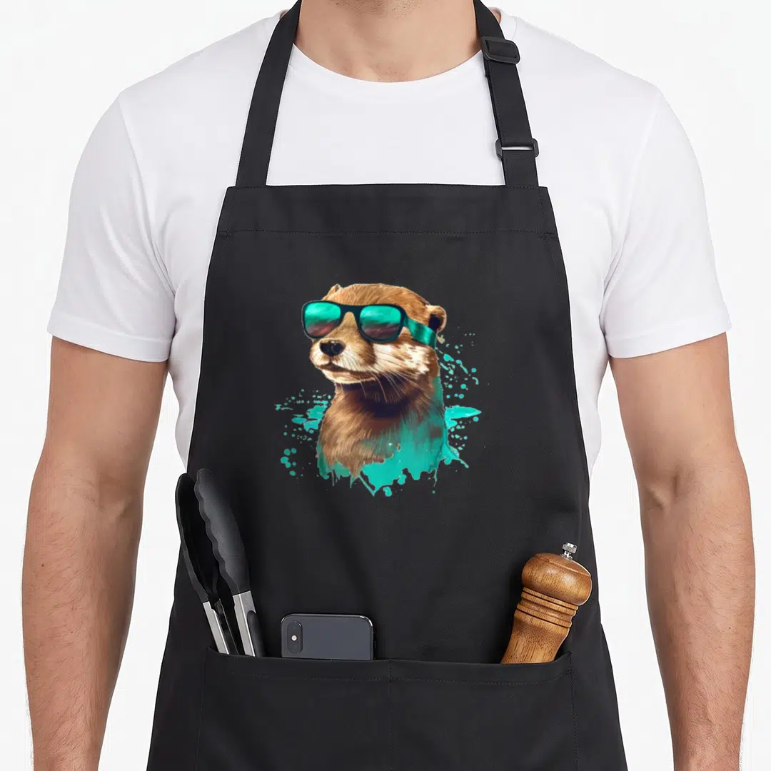 Funny otter sunglasses funny apron - Realistic brown otter head wearing sunglasses with teal paint splatters on a black — shown on a black cotton canvas apron against a white background