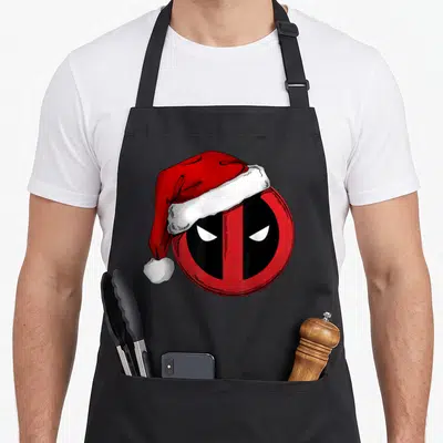 Icon santa aprons - Red and black Deadpool mask wearing a red and white Santa hat in cartoon style — shown on a black cotton canvas apron against a white background