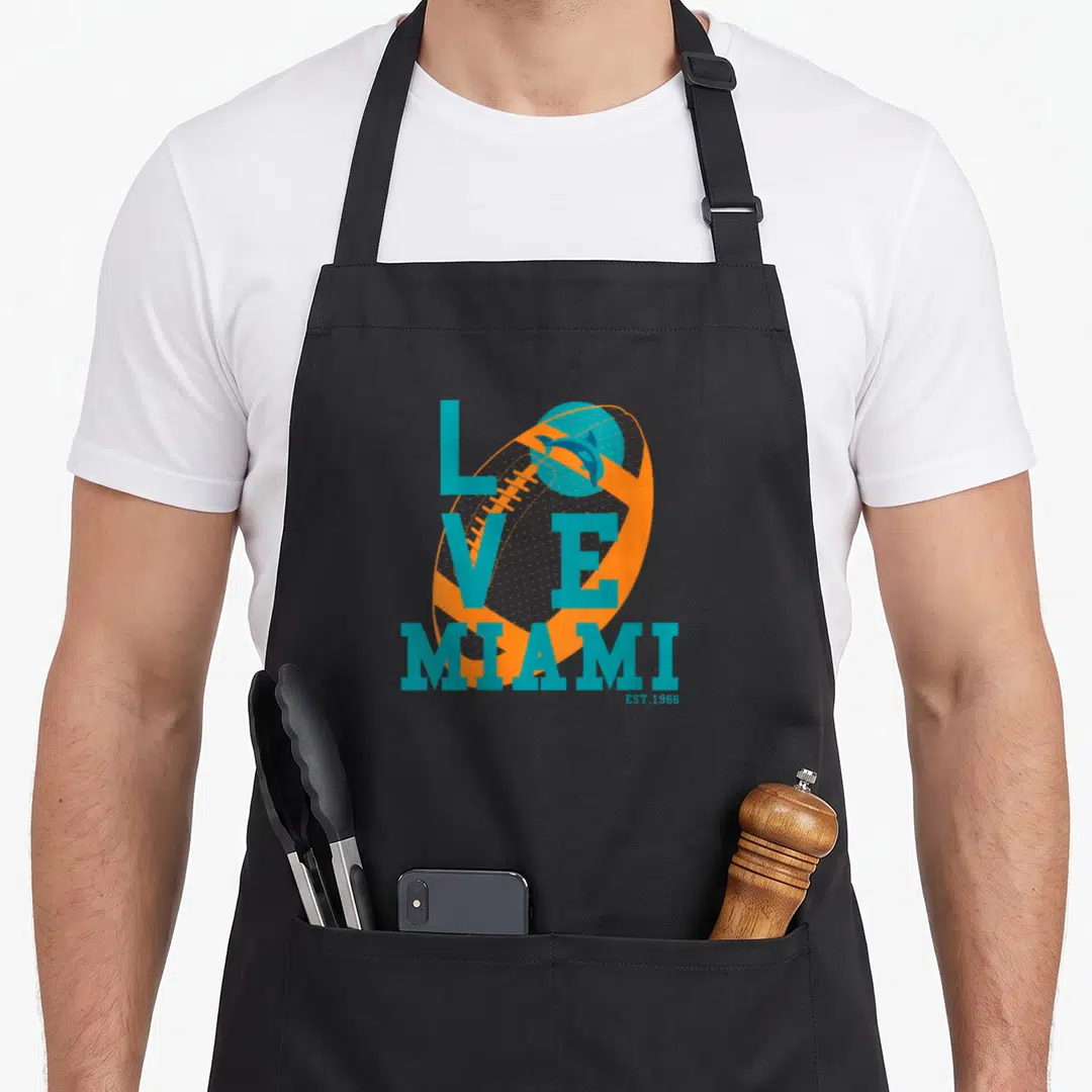 Miami sports team aprons - Orange football with teal LOVE MIAMI EST.1966 text and dolphin logo — shown on a black cotton canvas apron against a white background
