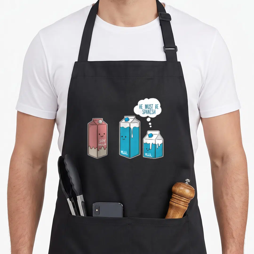 Soy spanish aprons - Three cartoon milk cartons in blue, pink, white with thought bubble text He Must Be Spanish — shown on a black cotton canvas apron against a white background