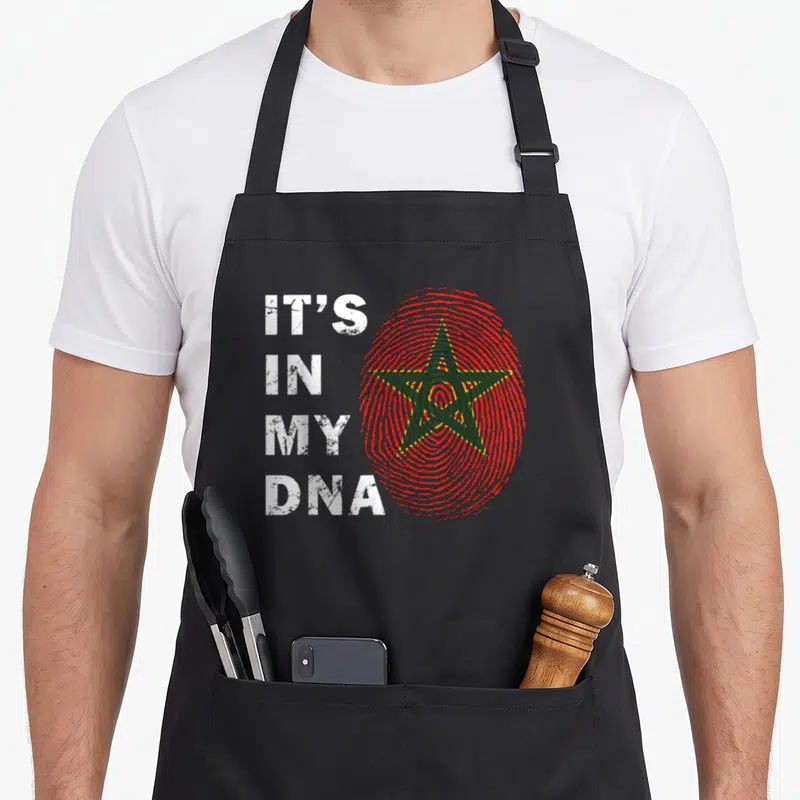 Dna moroccan girl apron - Red fingerprint with green star and white stacked text IT'S IN MY DNA distressed — shown on a black cotton canvas apron against a white background