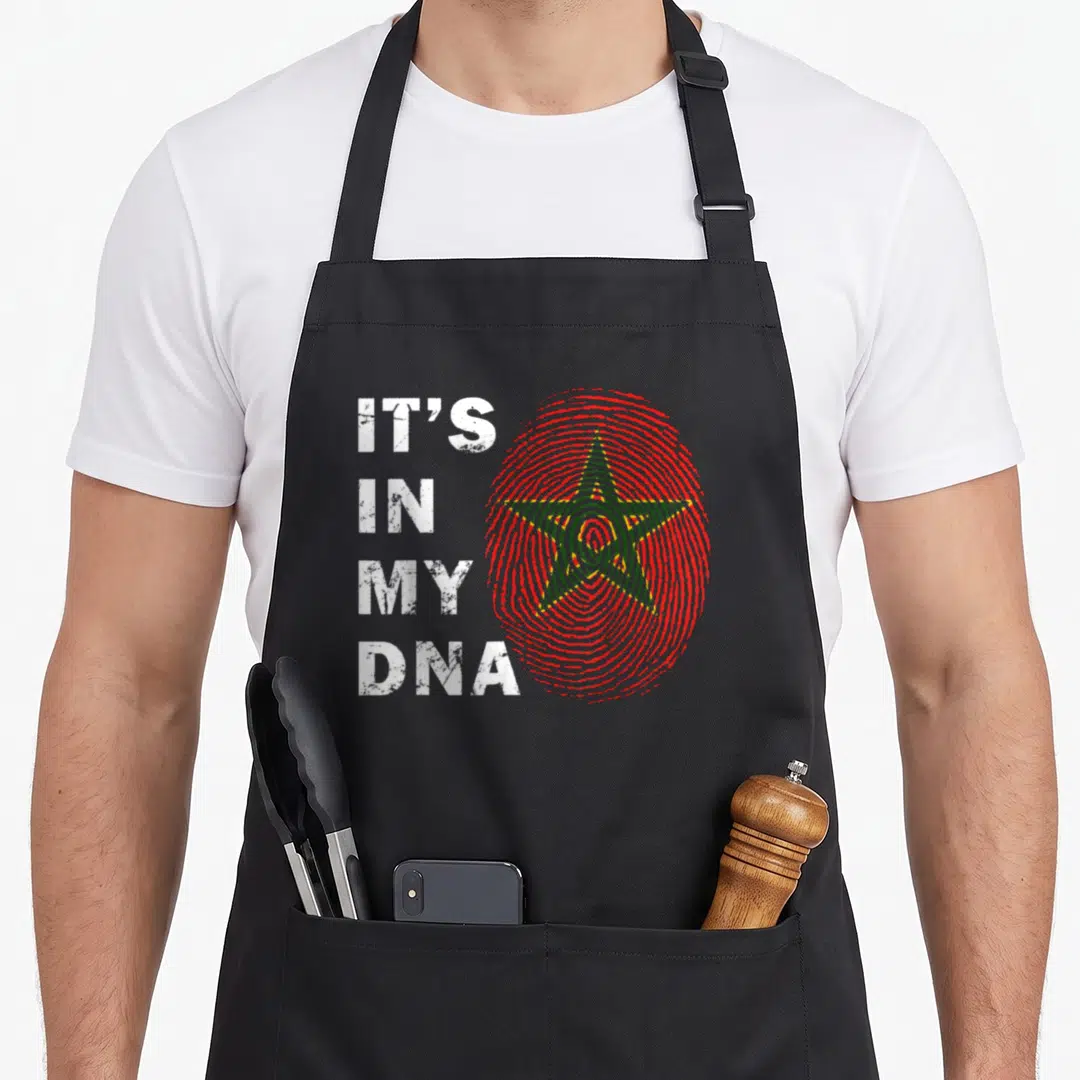 Dna moroccan girl apron - Red fingerprint with green star and white stacked text IT'S IN MY DNA distressed — shown on a black cotton canvas apron against a white background