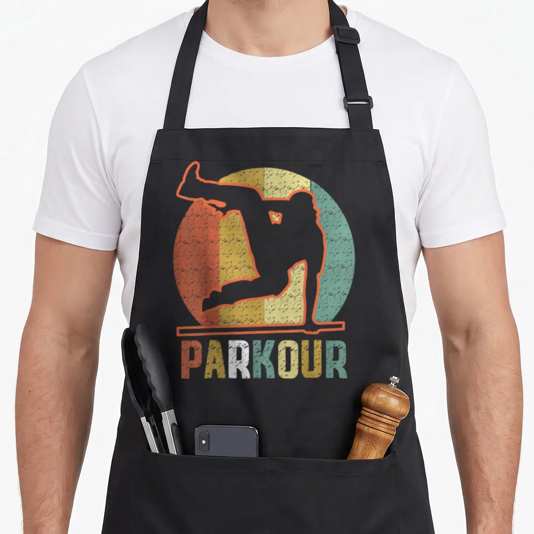 Funny parkour apron - Retro parkour athlete silhouette over a striped circle with multicolor PARKOUR text — shown on a black cotton canvas apron against a white background