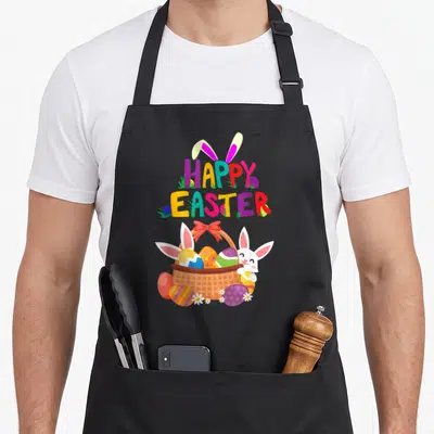 Cute easter apron - HAPPY EASTER text above basket with eggs and white bunny in pink yellow blue green orange — shown on a black cotton canvas apron against a white background